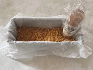 ラップを巻いた小瓶で型に敷いたクッキーを平らにする様子