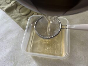 ゼラチン溶液茶こしで濾しながらタッパーに入れる様子