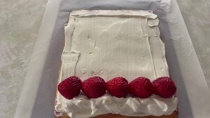 全体にクリームを塗り、巻き初めにいちごを並べたロール生地の写真